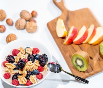 A nutritious breakfast bowl featuring fresh berries and walnuts, served with sliced fruit and kiwi.