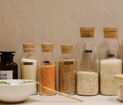 A variety of grains and pasta in labeled glass bottles displayed on a kitchen counter.